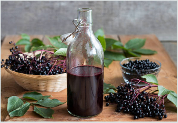 a bottle of homemade elderberry syrup and some elderberries on a wooden surface